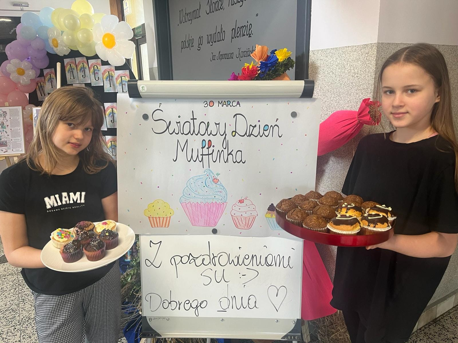 Uczennice samorządu uczniowskiego z muffinkami przy plakacie Światowy Dzień Muffina