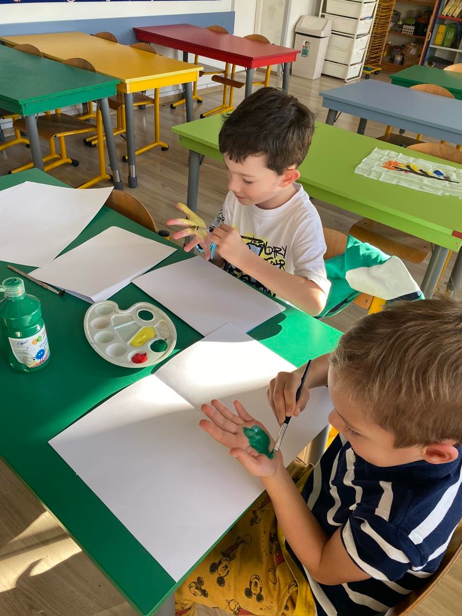 Uczniowie klasy 1j podczas zajęć plastycznych nakładają farbę starannie na swoje dłonie