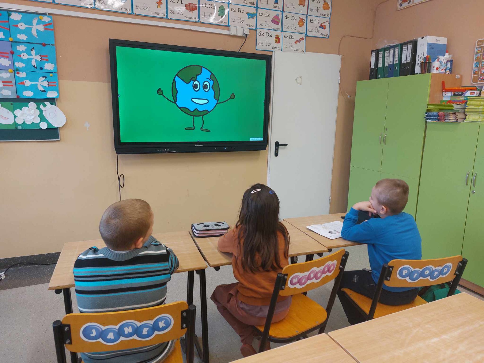 Uczniowie siedzą na krzesłach i oglądają film edukacyjny o Dniu Ziemi