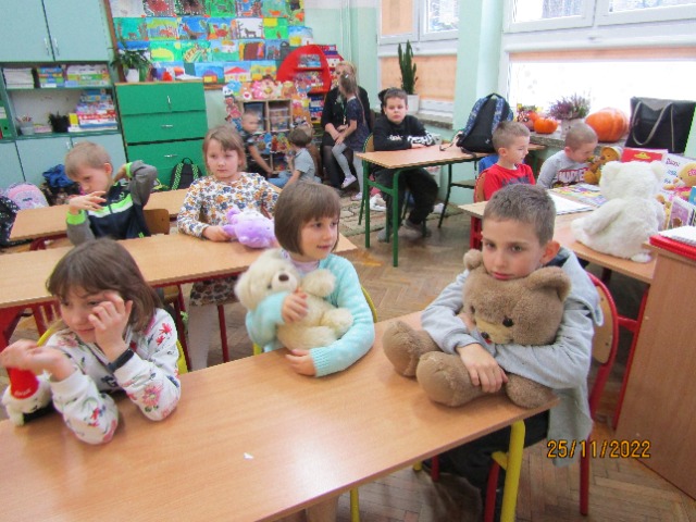 Sala lekcyjna, przy stolikach siedzą dzieci, w rękach trzymają pluszowe misie.