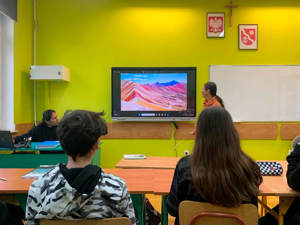 NNa zdjęciu zaproszeni goście przedstawiający slajdy i  opowiadający o życiu w Ameryce Południowej. Przed nimi siedzą uczniowie klasy ósmej.