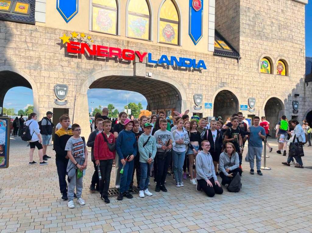 Na zdjęciu uczniowie klasy piątej, szóstej i siódmej na wycieczce stojący przed wejściem  do Energylandii. Wokół nich osoby, które wchodzą lub wychodzą z Energylandii.