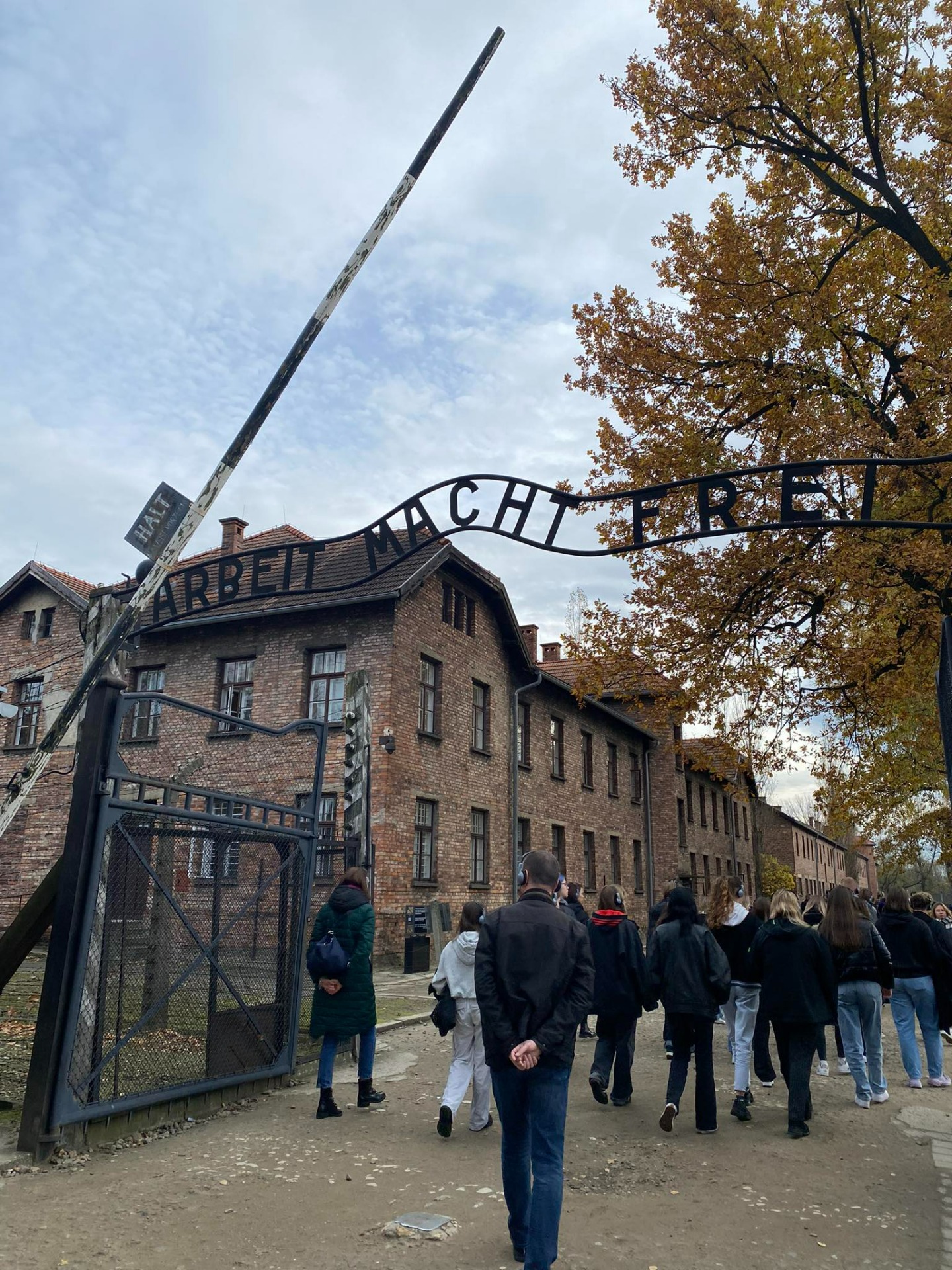 Młodzież przekraczająca bramę Auschwitz z napisem "Arbeit macht frei"