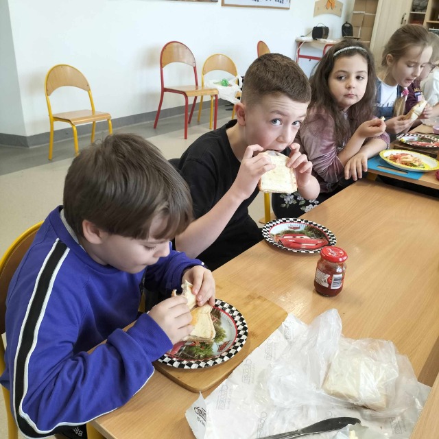 Uczniowie jedzą tosty przy stole.