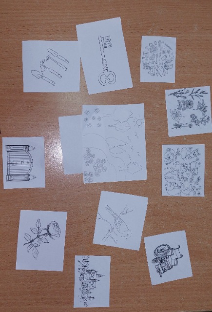 Na blacie leżą karteczki z wydrukowanymi rysunkami: kwiatów, narzędzi, bramy, ptaka.
