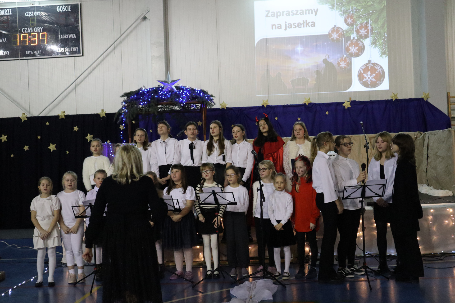 Uczniowie z chóru szkolnego podczas występu na tle scenografii świątecznej