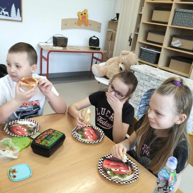 Uczniowie jedzą tosty przy stole.