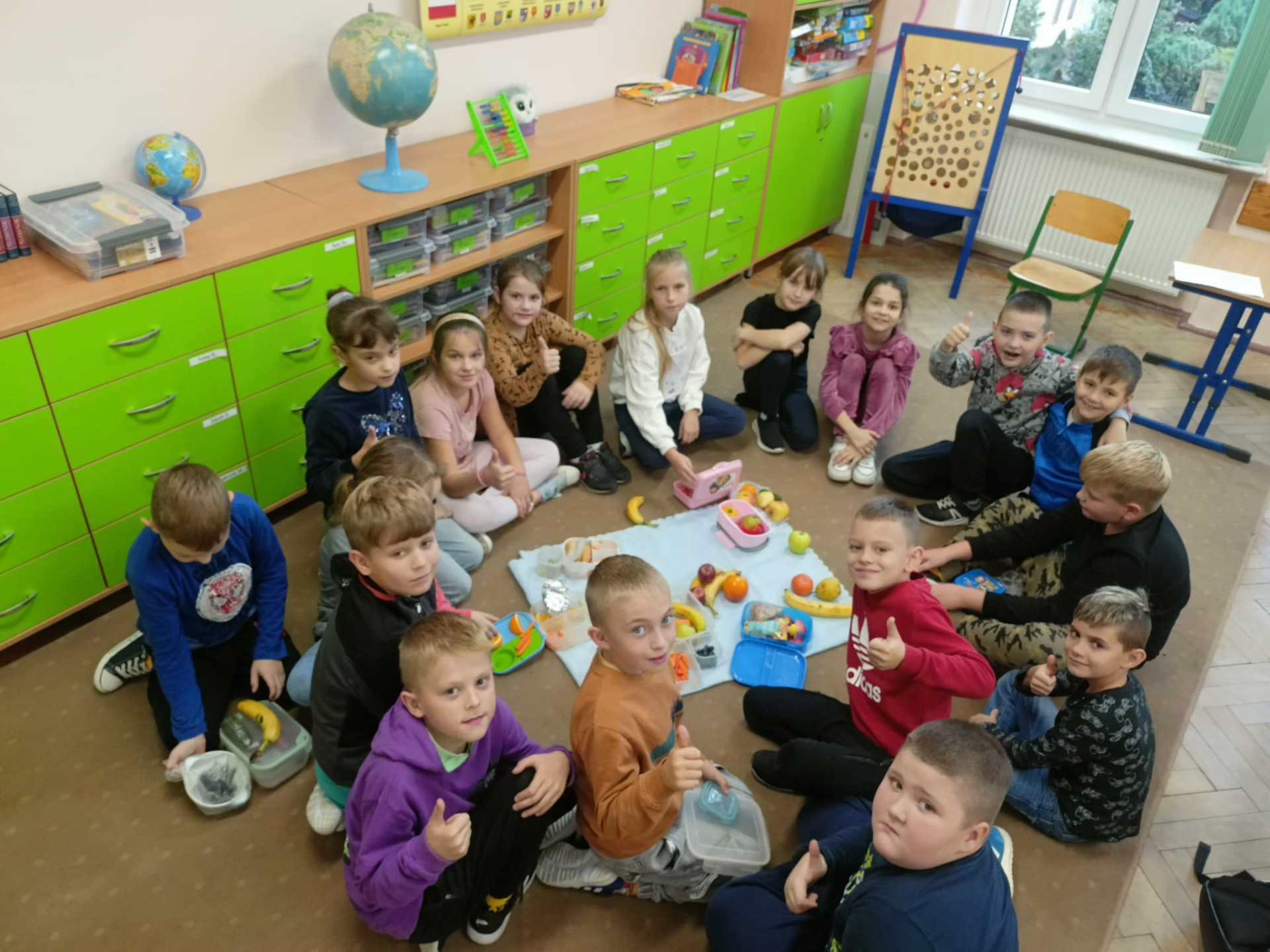Uczniowie siedzą na podłodze i spożywają zdrowe śniadanie.