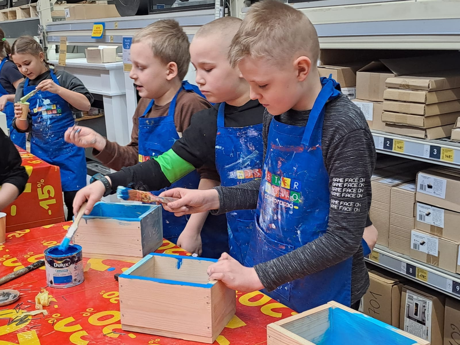 Uczniowie montują i malują drewniane pudełka podczas warsztatów w Castoramie.