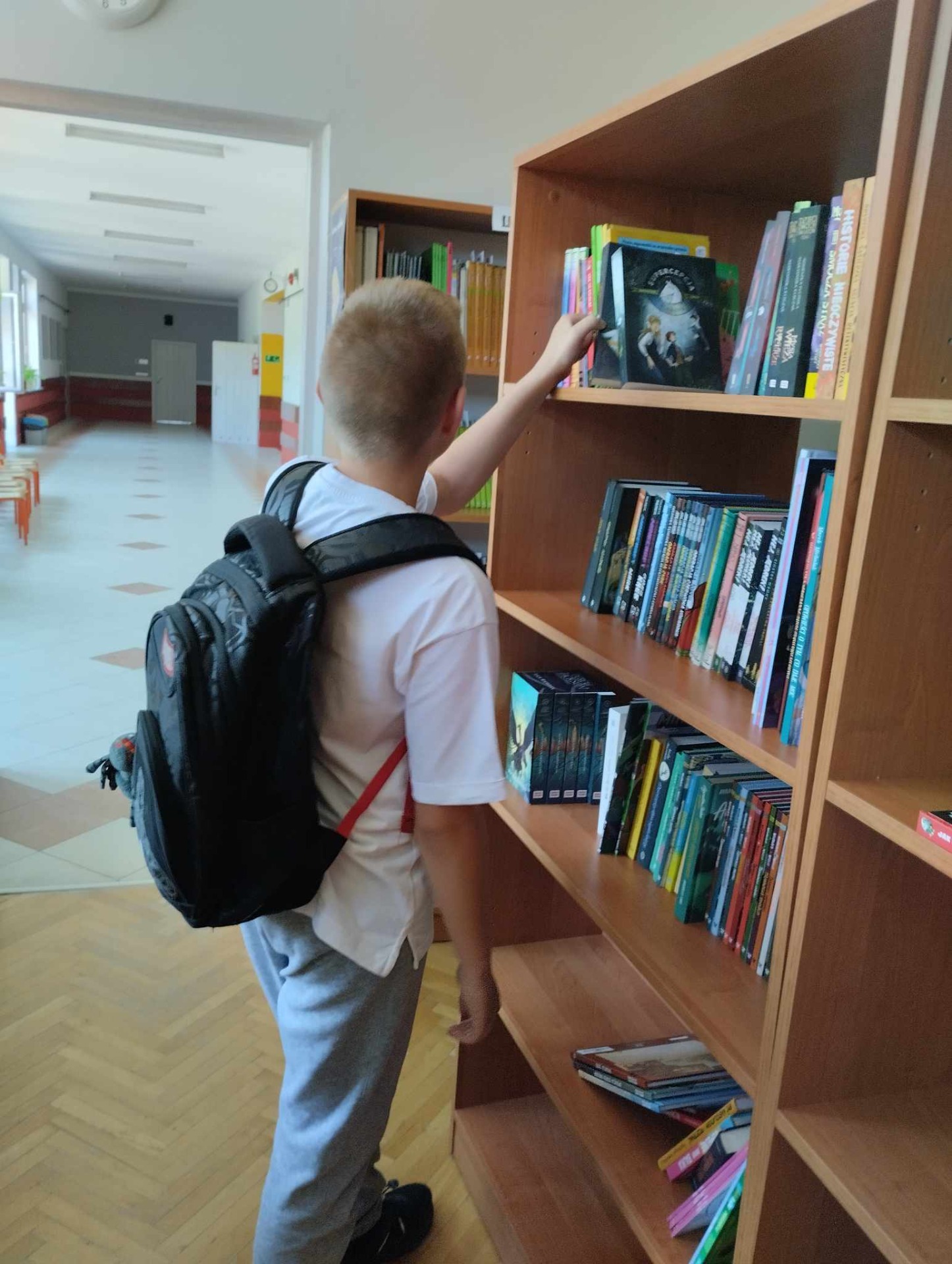Na zdjęciu uczeń szuka wśród książek ciekawej pozycji bibliotecznej na okres wakacyjny.